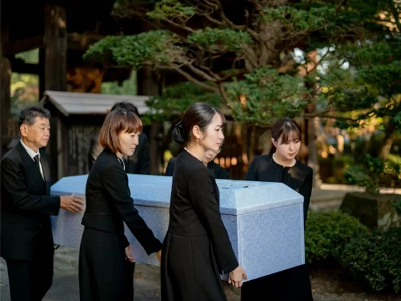 火葬場へ棺を運んでいる家族